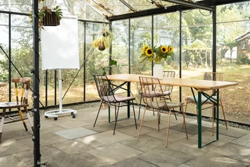 Tafels, stoelen met gekleurde poten, zonnebloemen en een flip-over in de verbouwde kas