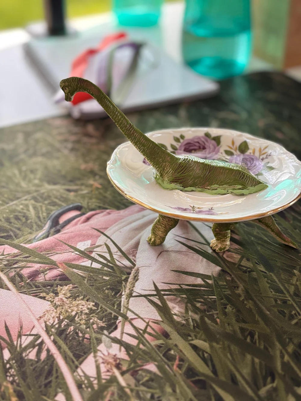 Een gebloemd bordje op de poten van een groene speelgoed-dinosaurus