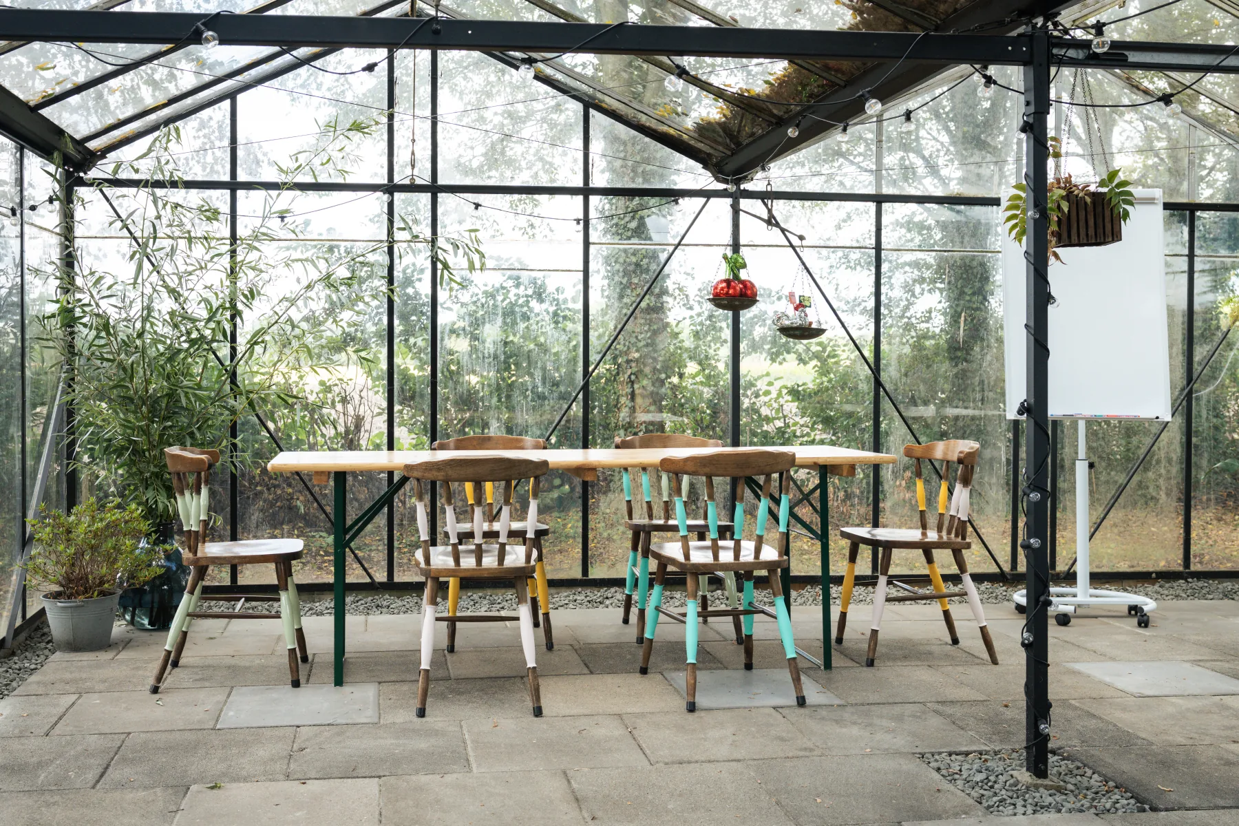 Lange tafel en stoelen in de lichte kas met uitzicht op het groen